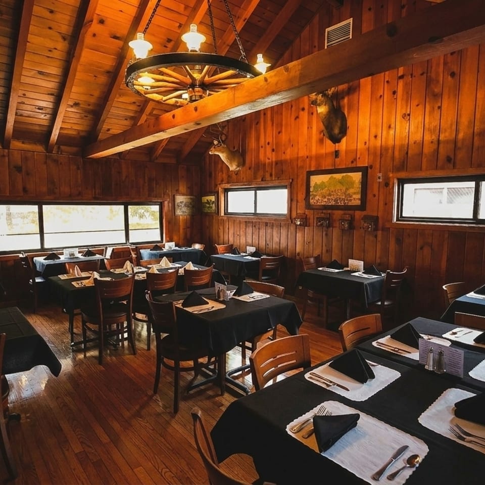 Rustic dining room with wood-paneled walls, antler decor, and tables set with black tablecloths.
