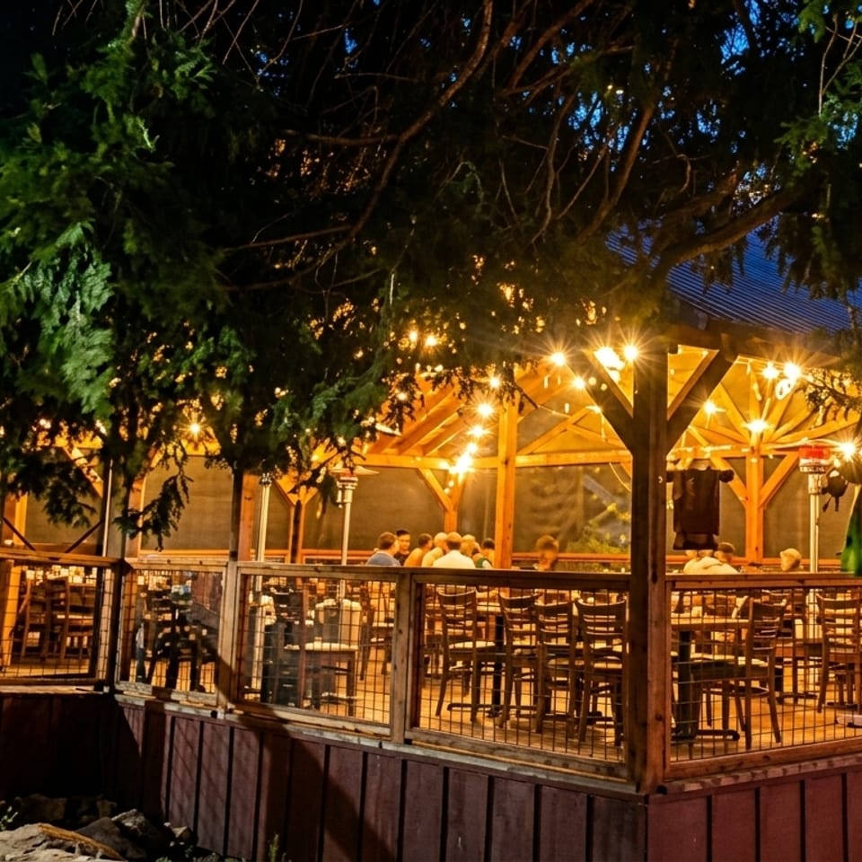 Outdoor restaurant patio at night, illuminated by string lights, with people dining at tables.