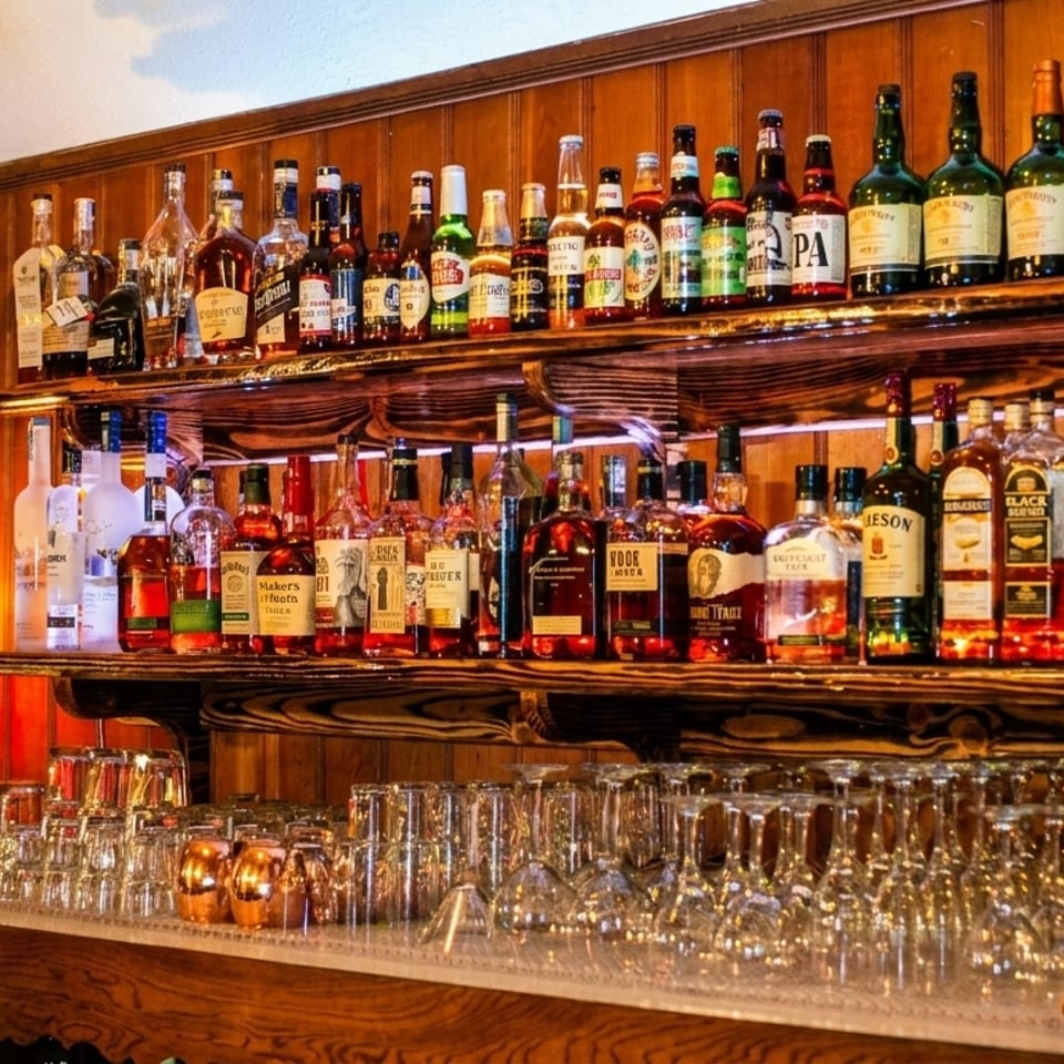 A rustic bar with shelves of liquor bottles, glasses, and a deer head wearing a headband.